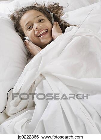 Stock Photograph - Young girl in bed listening to music. Fotosearch