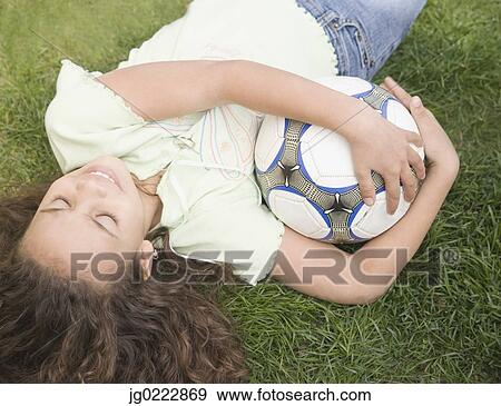 Stock Photo - Young girl laying on ground with soccer ball. Fotosearch