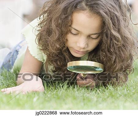 Stock Photo - Young girl looking through magnifying glass at grass. Fotosearch