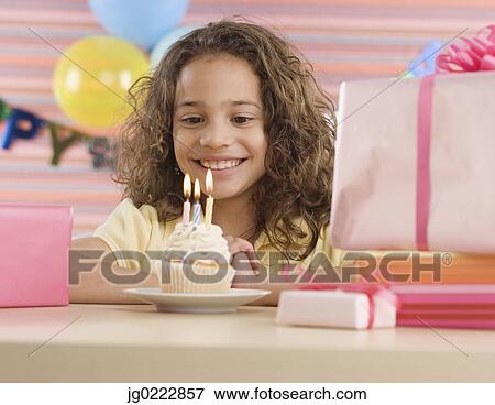 Stock Photo - Young girl with cupcake and lit candles at birthday party. Fotosearch