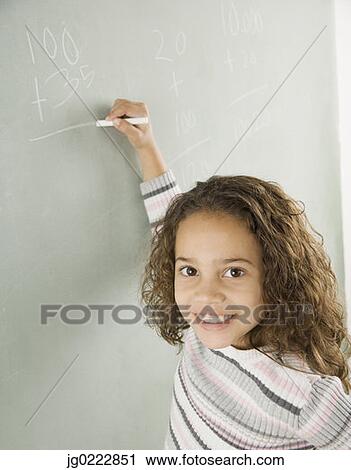 Stock Image - Young girl writing on blackboard in classroom. Fotosearch