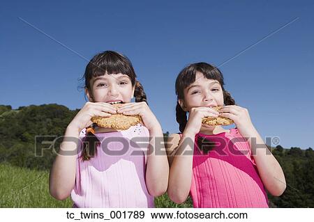 Stock Photo - Young Hispanic sisters eating cookies outdoors. Fotosearch