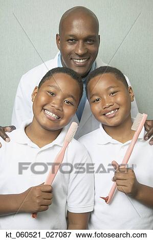 Stock Photo - African male dentist with twin boys holding toothbrushes. Fotosearch