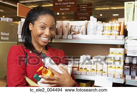 Picture - African woman at store with armful of products. Fotosearch