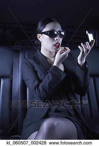 Stock Photo - Asian businesswoman applying make up in back seat of car. Fotosearch