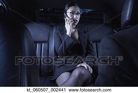 Stock Image - Asian businesswoman using cell phone in back seat of car. Fotosearch