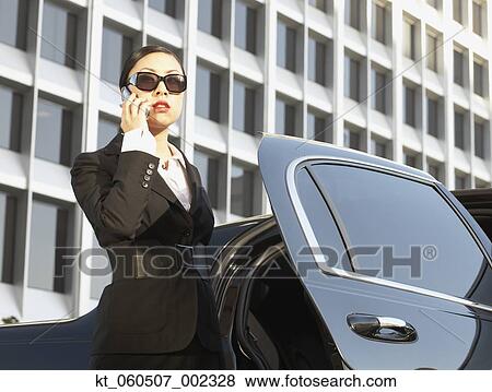 Stock Photo - Asian businesswoman using cell phone next to car. Fotosearch