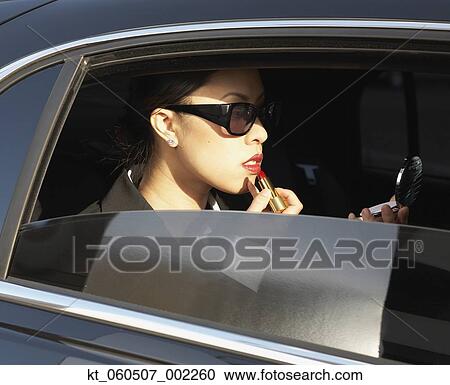 Asian woman applying lipstick in backseat of car View Large Photo Image Stock Image - Asian woman applying lipstick in backseat of car. Fotosearch