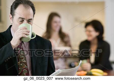 Stock Photo - Businessman drinking coffee with family in background. Fotosearch