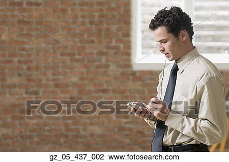 Stock Image - Businessman using PDA with head set. Fotosearch