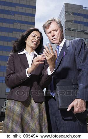 Picture - Businesswoman and businessman looking at PDA in urban scene. Fotosearch