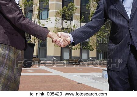 Stock Image - Businesswoman and businessman shaking hands outdoors. Fotosearch