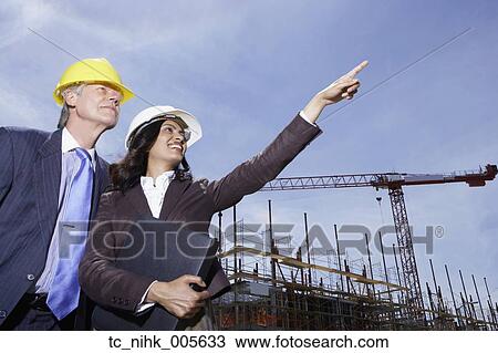 Stock Image - Businesswoman and businessman wearing hard hats at construction site. Fotosearch