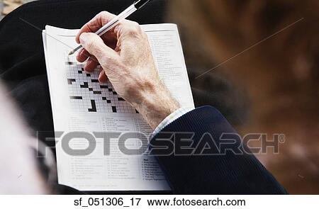 Stock Photo - Close up of senior man's hand with pen on crossword puzzle. Fotosearch