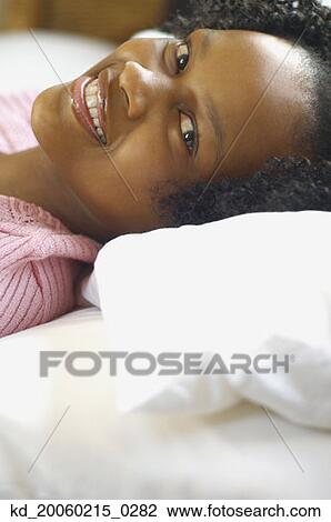 Stock Image - Close up of young African woman laying down and smiling. Fotosearch