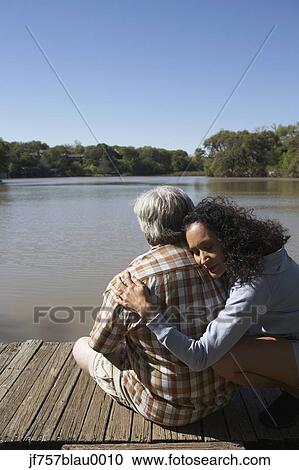 Stock Image - Couple hugging on wooden dock. Fotosearch