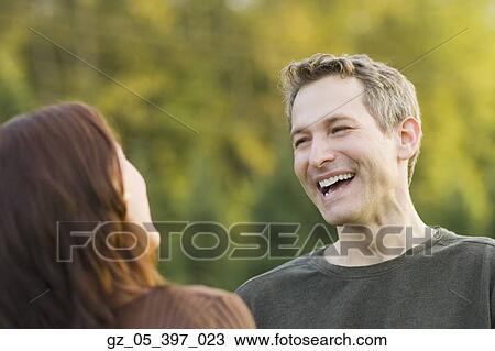 Stock Image - Couple looking at each other and laughing outdoors. Fotosearch