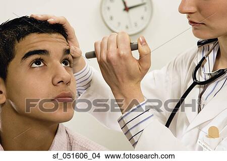 Female doctor checking young male patient's eye View Large Photo Image Picture - Female doctor checking young male patient's eye. Fotosearch