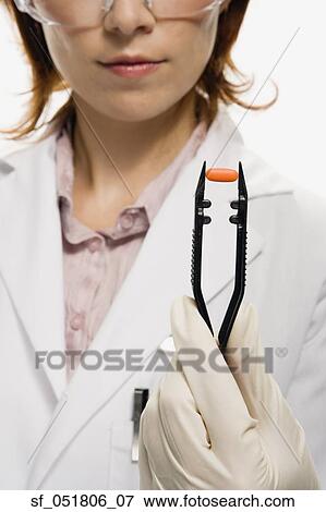 Stock Photo - Female lab technician holding pill in large tweezers. Fotosearch