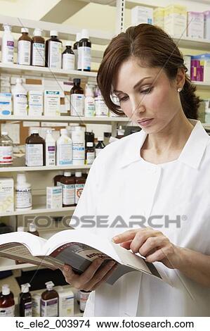 Picture - Female pharmacist looking at book in pharmacy. Fotosearch