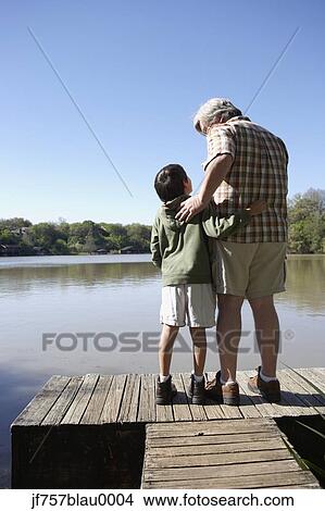Picture - Grandfather and grandson standing on wooden dock. Fotosearch