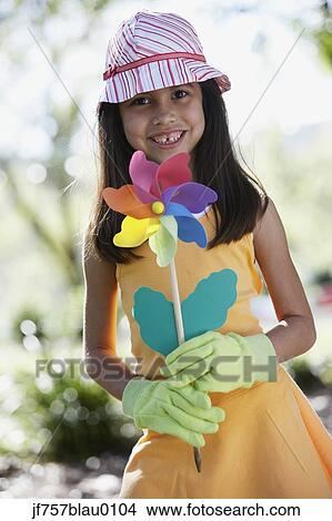 Picture - Hispanic girl holding flower pinwheel outdoors. Fotosearch