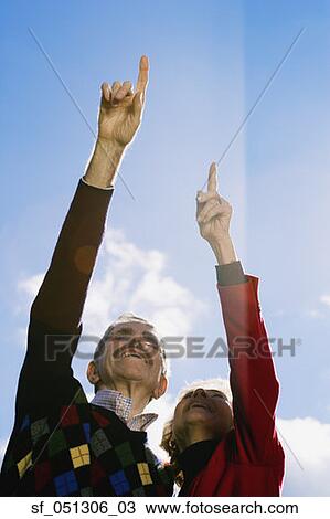 Stock Image - Low angle view of senior couple pointing outdoors. Fotosearch