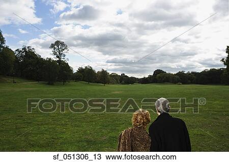 Stock Image - Rear view of senior couple looking out over open meadow. Fotosearch