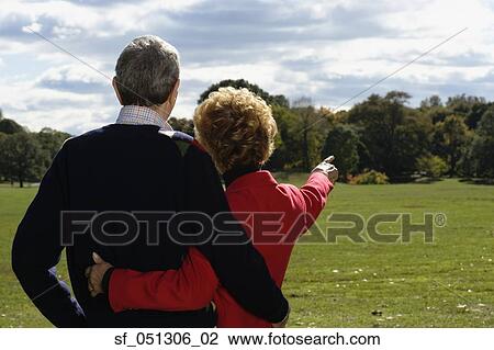 Stock Image - Senior couple hugging and pointing at park. Fotosearch