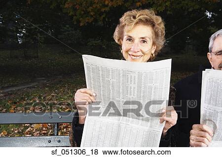 Stock Photo - Senior couple reading newspapers on bench outdoors. Fotosearch