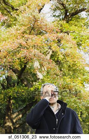 Stock Image - Senior man taking photograph outdoors. Fotosearch