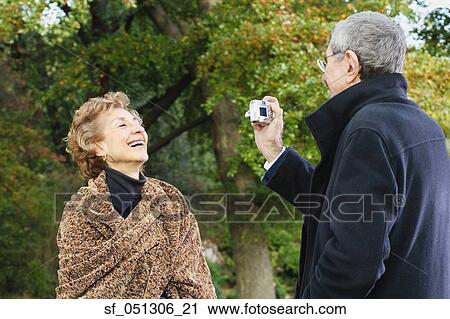Stock Image - Senior man talking senior woman's photograph outdoors. Fotosearch