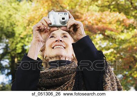 Stock Photograph - Senior woman taking photograph outdoors. Fotosearch