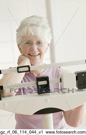 Stock Image - Senior woman weighing self on scale. Fotosearch