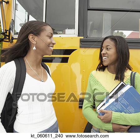 Stock Image - Two young African women next to school bus talking. Fotosearch