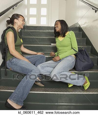 Stock Image - Two young African women talking on stairs at school. Fotosearch