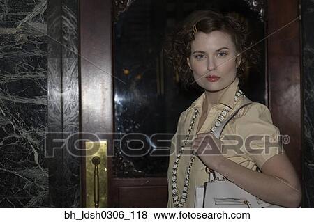 Stock Photo - Woman holding purse next to doorway. Fotosearch
