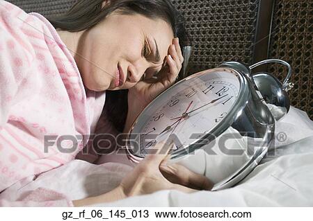 Stock Image - Woman laying in bed with giant alarm clock. Fotosearch