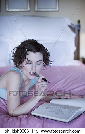 Stock Photography - Woman laying on bed with pen and book. Fotosearch