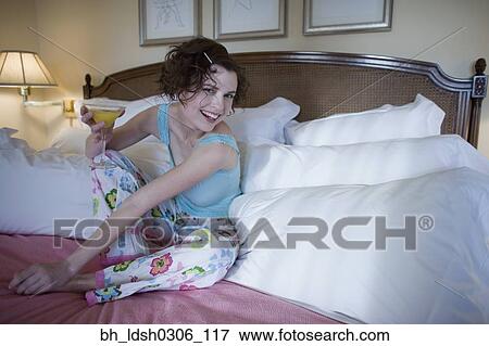 Stock Photo - Woman sitting on bed with cocktail. Fotosearch