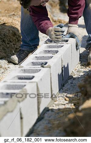 Stock Image - Worker filling cinder blocks with mortar. Fotosearch