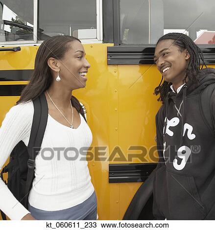 Stock Image - Young African couple leaning against school bus talking. Fotosearch