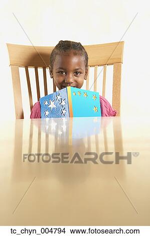 Picture - Young African girl holding book at table. Fotosearch