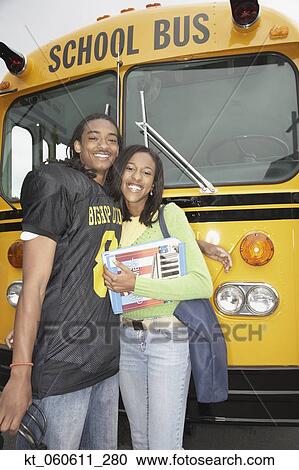 Stock Image - Young African man in football uniform with girlfriend next to school bus. Fotosearch