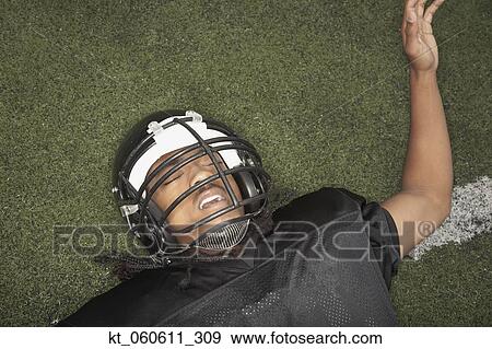 Stock Photo - Young African man in football uniform laying on field. Fotosearch