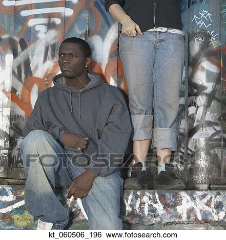 Young African man sitting against graffitied wall View Large Photo Image Stock Photograph - Young African man sitting against graffitied wall. Fotosearch