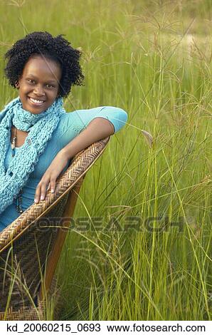 Young African woman sitting in chair in field View Large Photo Image Stock Image - Young African woman sitting in chair in field. Fotosearch