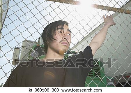 Young Asian man leaning against metal fence View Large Photo Image Stock Image - Young Asian man leaning against metal fence. Fotosearch