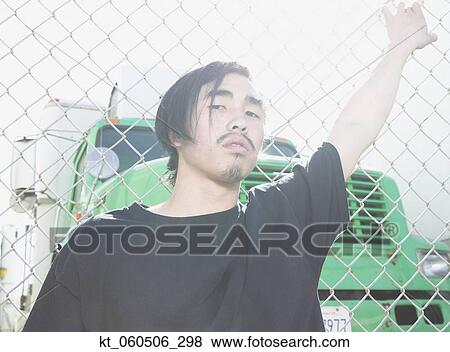Young Asian man leaning against metal fence View Large Photo Image Stock Photo - Young Asian man leaning against metal fence. Fotosearch