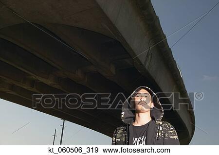 Stock Photo - Young Asian man standing under raised highway. Fotosearch